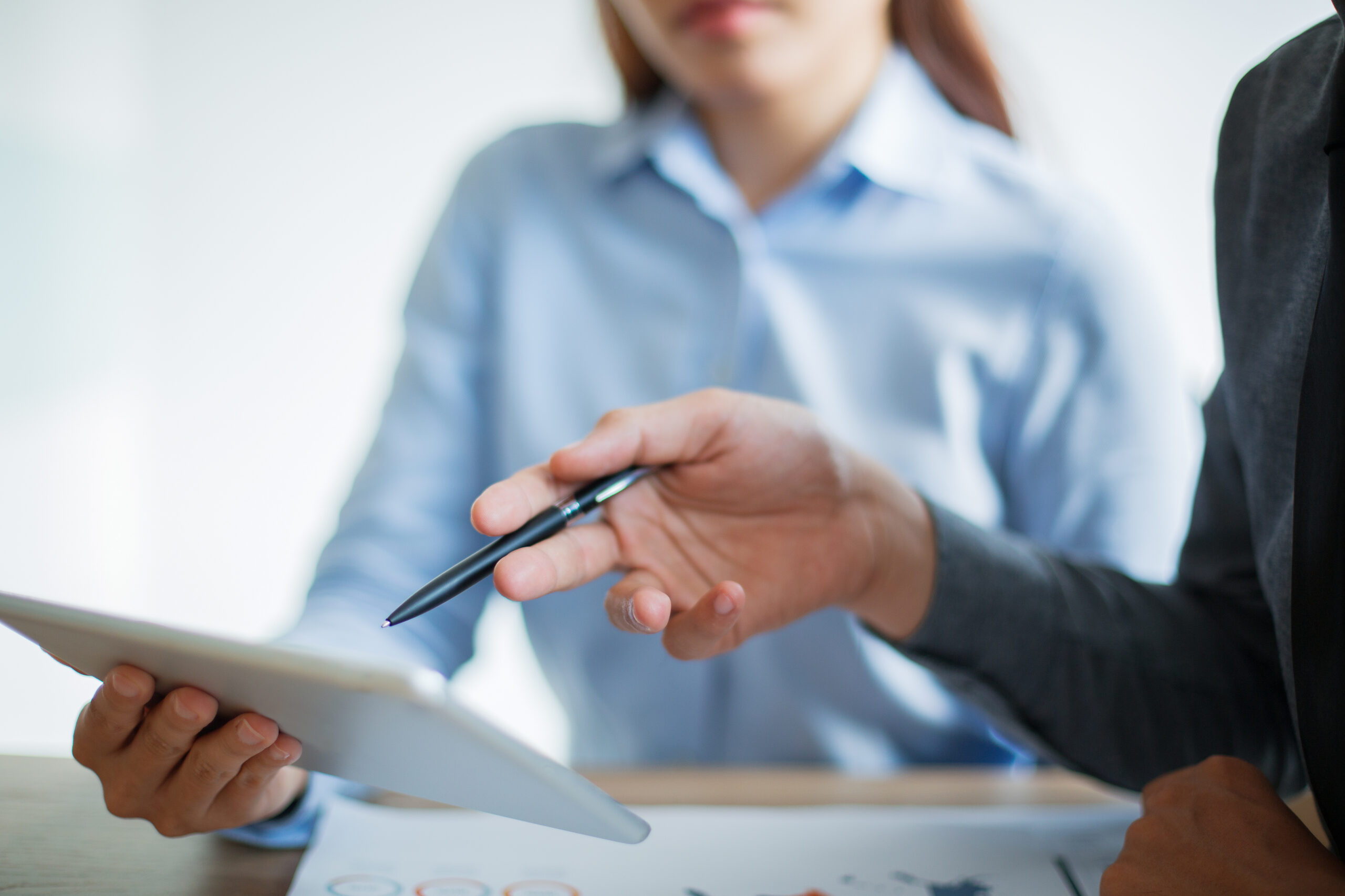 Unrecognizable Asian business team having meeting in office. Businesswoman holding touchpad, businessman pointing at touchscreen with pen and discussing information
